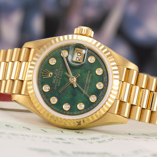 Gold wristwatch with a green face on a marble surface
Rolex, Datejust, Bloodstone Dial, Yellow Gold